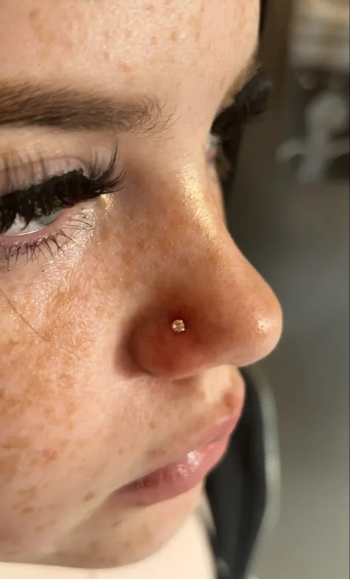 Healed gold nostril stud on a freckled client